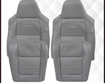 May include: Two gray vinyl car seat covers with the word "TAIRAJ" embroidered on the headrests. The covers are made in the USA.  "AUTO SEAT REPLACEMENT" and "Vinyl" are printed on the image.