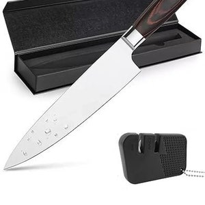 May include: A black and brown handled chef's knife with a stainless steel blade. The knife is in a black box with a black and white patterned lining. A black knife sharpener is also included.