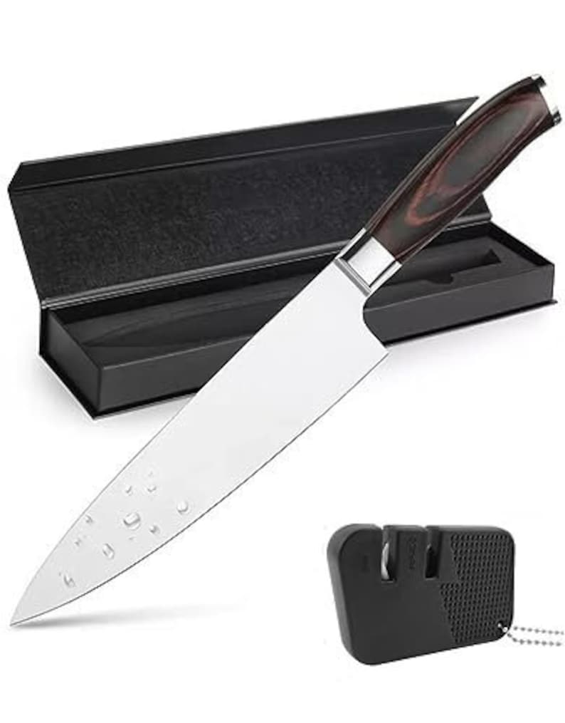 May include: A black and brown handled chef's knife with a stainless steel blade. The knife is in a black box with a black and white patterned lining. A black knife sharpener is also included.