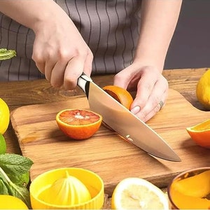 May include: A person is using a silver kitchen knife to cut a red orange on a wooden cutting board. There are other oranges and lemons on the board.