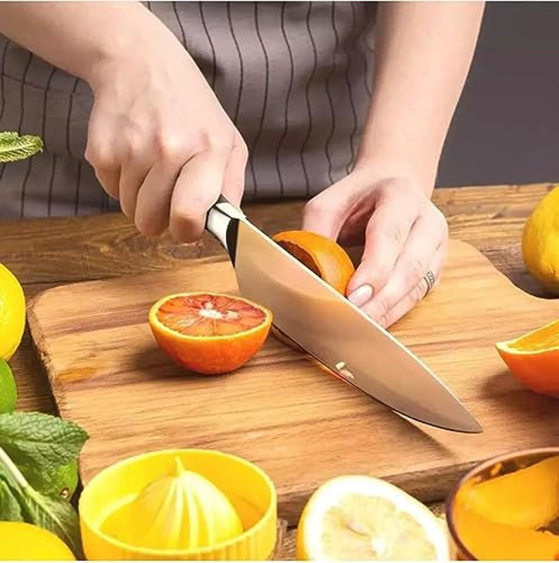 May include: A person is using a silver kitchen knife to cut a red orange on a wooden cutting board. There are other oranges and lemons on the board.