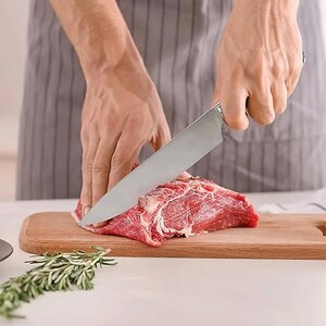 May include: A person is using a silver knife to cut a piece of raw red meat on a wooden cutting board.
