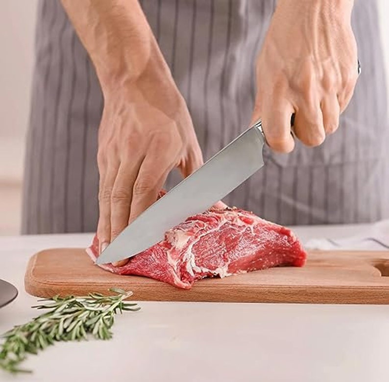 May include: A person is using a silver knife to cut a piece of raw red meat on a wooden cutting board.