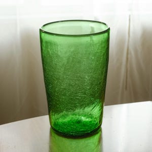 May include: A tall, green glass with a textured surface. The glass has a cylindrical shape and a slightly flared rim. The color is a vibrant, transparent green, suitable for serving beverages.