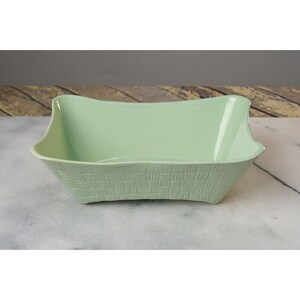 May include: A light green ceramic serving bowl with a woven pattern. The bowl has a rectangular shape with rounded edges.
