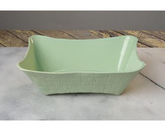 May include: A light green ceramic serving bowl with a woven pattern. The bowl has a rectangular shape with rounded edges.