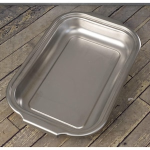 May include: A rectangular, stainless steel baking pan with a slightly raised rim and handles. The pan has a smooth, reflective surface and is designed for baking and cooking. The pan is shown on a wooden surface.
