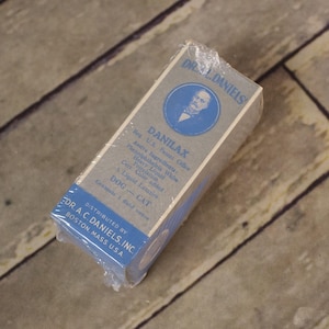 May include: A vintage Danilax box, wrapped in cellophane. The box is gray and blue, with text including "DANILAX" and "DOG - CAT". The box is distributed by Dr. A.C. Daniels, Inc. of Boston, Mass. U.S.A.