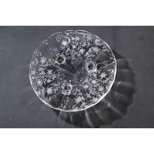 May include: A clear glass cake stand with a floral pattern and three feet.