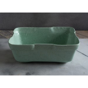 May include: A light green ceramic baking dish with a speckled finish. The dish has a rectangular shape with slightly rounded edges.