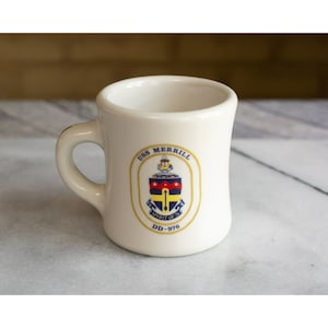 May include: White ceramic mug with a navy blue and yellow crest featuring the text "USS MERRILL SPIRIT OF 76 DD-976".