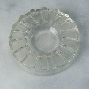 May include: A clear glass ashtray with a scalloped edge and a textured design.