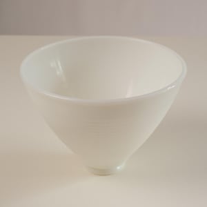 May include: A white, cone-shaped bowl with a wide rim. The bowl has a smooth, glossy finish and a subtle textured band around the middle. The bowl's design is simple and elegant, suitable for serving various dishes.