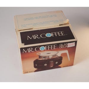 May include: A vintage Mr. Coffee glass decanter with handle and lid, in its original box. The box features the Mr. Coffee logo and product details. The decanter is brown with white accents.