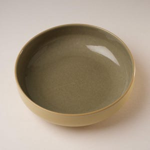 May include: A large, round, ceramic bowl with a light green interior and a yellow rim.