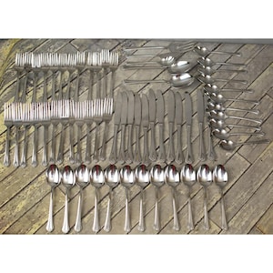 May include: A complete set of silver-colored flatware, including forks, knives, and spoons, arranged on a wooden surface. The silverware has a decorative floral design on the handles. The set includes multiple place settings.
