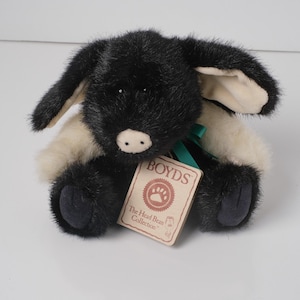 May include: A plush black and white dog toy with floppy ears and a green ribbon. The toy has a tag that reads "BOYDS The Head Bean Collection". The dog has black paws and a light pink nose.