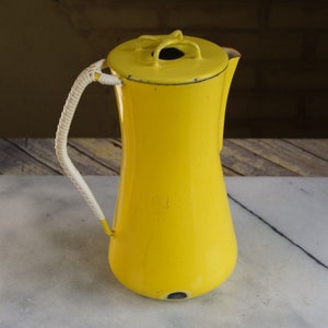 May include: A bright yellow enamel coffee pot with a white woven handle. The pot has a round lid with a small hole in the center.