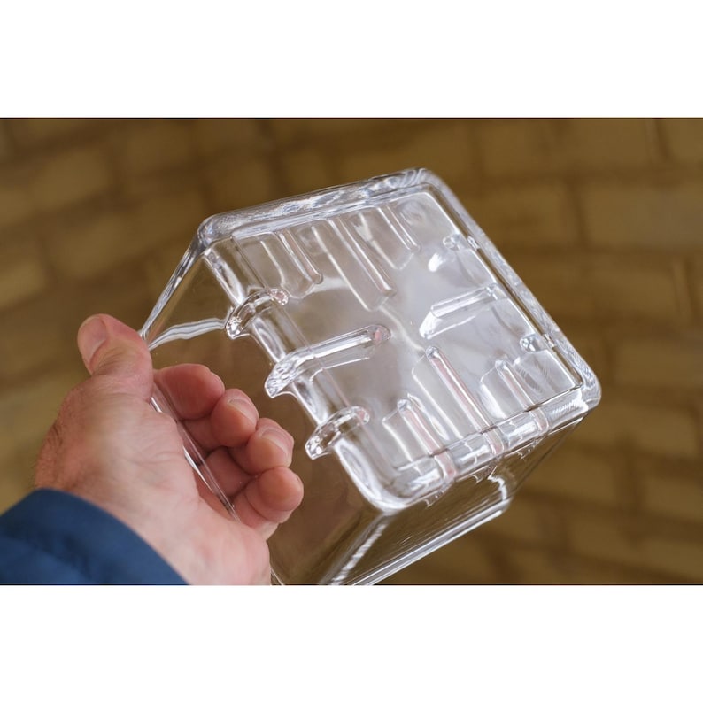 Pu&ograve; includere: Un contenitore di plastica trasparente di forma quadrata con coperchio. Il contenitore ha una superficie strutturata ed &egrave; tenuto da una persona. Il coperchio presenta creste e scanalature in rilievo. Per la conservazione degli alimenti.