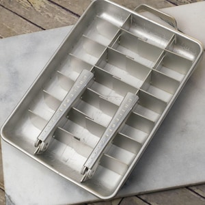 May include: A vintage silver ice cube tray with two removable handles. The tray has 12 individual ice cube molds.