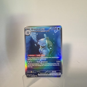 May include: A holographic Blastoise EX Pokémon card. The card features a blue Blastoise character with a water background. The card text includes "Twin Cannons" and "Solid Shell" abilities, along with the number 330.