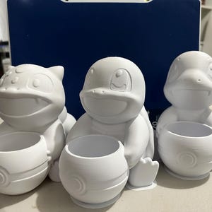 Peut inclure: Trois pots de fleurs en céramique blanche en forme de personnages Pokémon. Les pots sont non peints et prêts à être décorés.