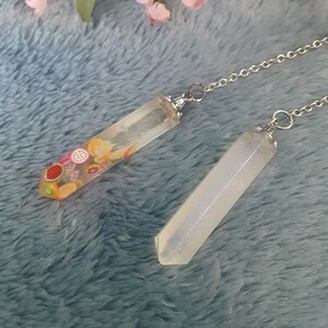 May include: Two clear crystal pendants on a silver chain. One pendant is filled with colorful fruit slices, the other is clear with glitter.