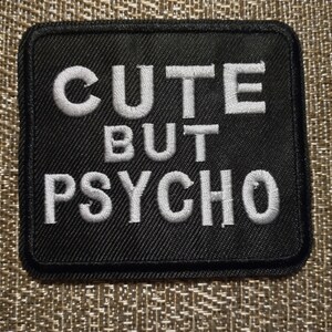 May include: Black fabric patch with white embroidered text that reads "Cute But Psycho".