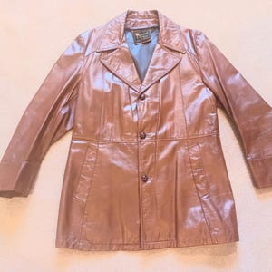 May include: A brown leather jacket with a button-up front and a collar. The jacket has a label that reads "Mr.  Ward" on the inside.