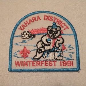 May include: Embroidered patch with a blue border, featuring a bear wearing sunglasses, a hat, and a scarf. The patch includes the text "YAHARA DISTRICT WINTERFEST 1991" in pink and blue, along with an igloo and a fleur-de-lis.
