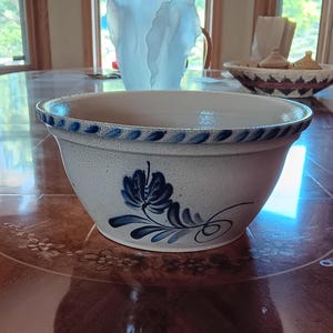 May include: A large white ceramic bowl with a blue and white floral design. The bowl has a blue rim and a blue and white floral pattern on the side.
