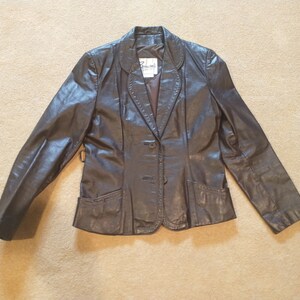 May include: A brown leather blazer with a single button closure and two pockets. The blazer has a  "Renowned" label on the inside.