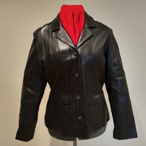 May include: A black leather jacket with a button closure and a single pocket on the front. The jacket has a collar and long sleeves.
