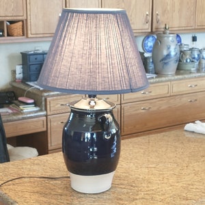 May include: A blue and white ceramic lamp base with a gray fabric lampshade. The lamp is on a granite countertop.