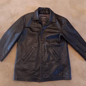 May include: A black leather jacket with a button-up front and two pockets. The jacket has a label that reads "The Sak's Fifth Avenue".