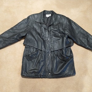 May include: A black leather jacket with a zipper closure, a drawstring waist, and two flap pockets. The jacket has a collar and a long sleeve.
