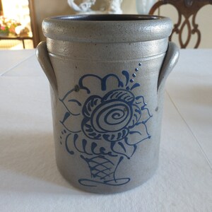 May include: A gray stoneware crock with a blue and white floral design. The crock has two handles and a wide mouth.