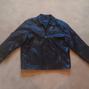 May include: Black leather jacket with a collared neckline, a zipper closure, and two front pockets. The jacket has long sleeves and is laid flat on a neutral surface. The jacket is a classic outerwear piece.