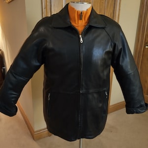 May include: A black leather jacket with a zipper closure and two zippered pockets. The jacket has a stand-up collar and a contrasting orange lining.