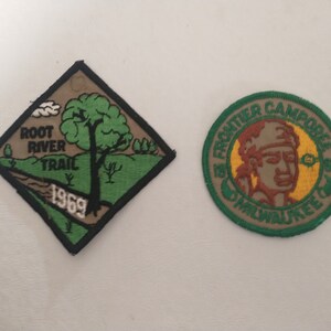 May include: Two vintage patches. One is a diamond shape with a green border, featuring a tree and the text "Root River Trail 1969." The other is a circular patch with a Native American profile and the text "St. Frontier Camporee Milwaukee."