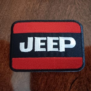 May include: A red, white, and black embroidered patch with the word "JEEP" in white lettering.