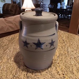 May include: A gray ceramic crock with a blue lid and three blue stars on the side. The crock is sitting on a granite countertop.