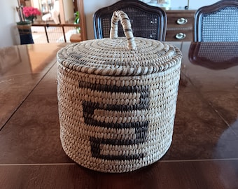 May include: A woven basket with a lid and a handle. The basket is made of natural materials and has a brown and white pattern.