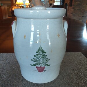 May include: White ceramic cookie jar with a green Christmas tree design and red pot. The jar has two handles and a lid.