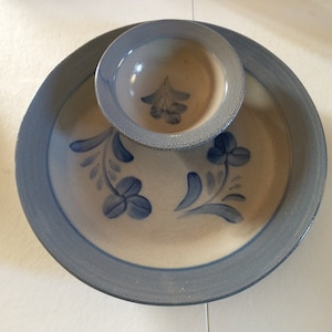 May include: A ceramic serving dish with a smaller bowl in the center. The dish is decorated with blue floral designs on a beige background. The rim of the dish is a light blue color.