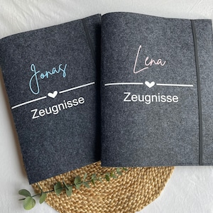 Könnte beinhalten: Zwei graue Filzordner mit weißem Text und einem kleinen Herz. Der Ordner links sagt "Jonas Zeugnisse" und der Ordner rechts sagt "Lena Zeugnisse".