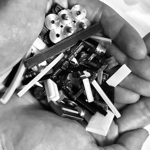 Könnte beinhalten: Eine Sammlung kleiner, schwarzer, weißer und silberner Kunststoff- und Metallteile. Die Teile befinden sich in der Hand einer Person.