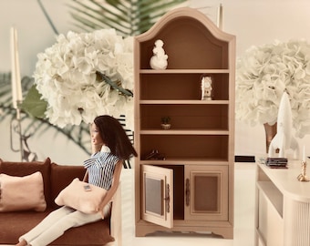 May include: A light brown wooden bookcase with four shelves and a cabinet with two doors. The cabinet doors have glass panels. The bookcase is decorated with a white figurine, a clock, and a small potted plant.