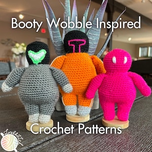Puede incluir: Tres juguetes amigurumi de crochet, uno gris, uno naranja y uno rosa, con el texto "Booty Wobble Inspired Crochet Patterns" en la parte superior de la imagen.