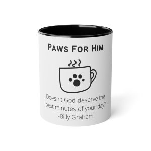 May include: White ceramic coffee mug with a black rim and handle. The mug has a black paw print design and the text "PAWS FOR HIM" and "Doesn't God deserve the best minutes of your day? -Billy Graham".